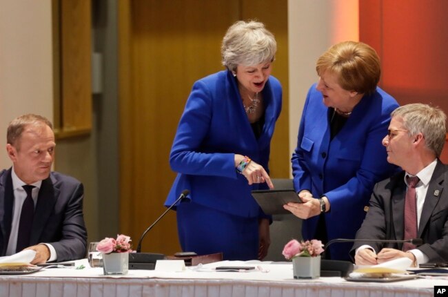 European Council President Donald Tusk, left, looks on as British Prime Minister Theresa May, center left, and German Chancellor Angela Merkel, center right, view a tablet during a meeting at an EU summit in Brussels, April 10, 2019.