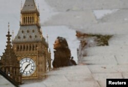 A woman is reflected in a puddle as she walks near the Houses of Parliament in central London, June 23, 2016.