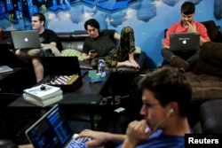 Zander Dejah (2nd L), 25, who works as a Virtual Reality engineer, Nick Olszowy (C), 25, a software engineer and Andrew Bresee, 26, a software engineer, all who are residents of The Negev tech house, use their electronics during a Sunday "family" dinner i