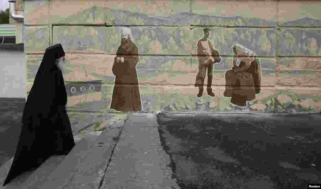 Orthodox monk Father Ioakim, 74, looks at a street graffiti, which displays Siberian characters of the 19th century including an Russian Orthodox monk, in Divnogorsk town outside Russia's Siberian city of Krasnoyarsk, Russia.