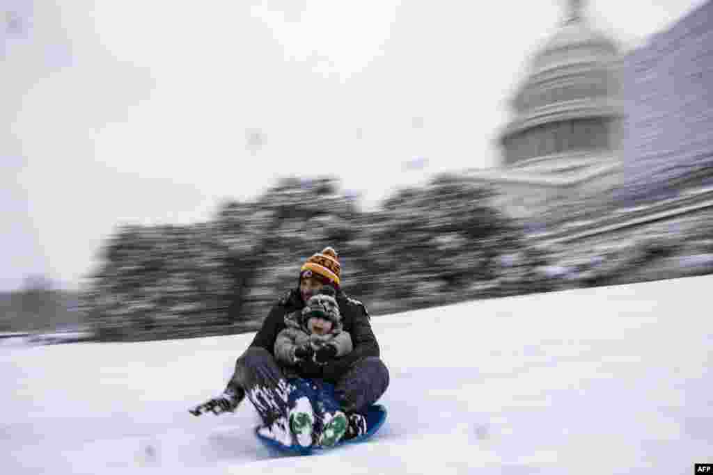 Seorang ayah dan putranya bermain papan seluncur di dekat Gedung Capitol ketika salju turun di Washington DC.