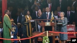 Rais Uhuru Kenyatta akishikilia biblia na mkono wake wa kulia wakati akiapishwa kuwa rais wa nne wa Jamhuri ya Kenya katika uwanja wa Kasarani Sports Center huko Nairobi, Kenya akiangaliwa mke wake Margaret Uhuru kulia .