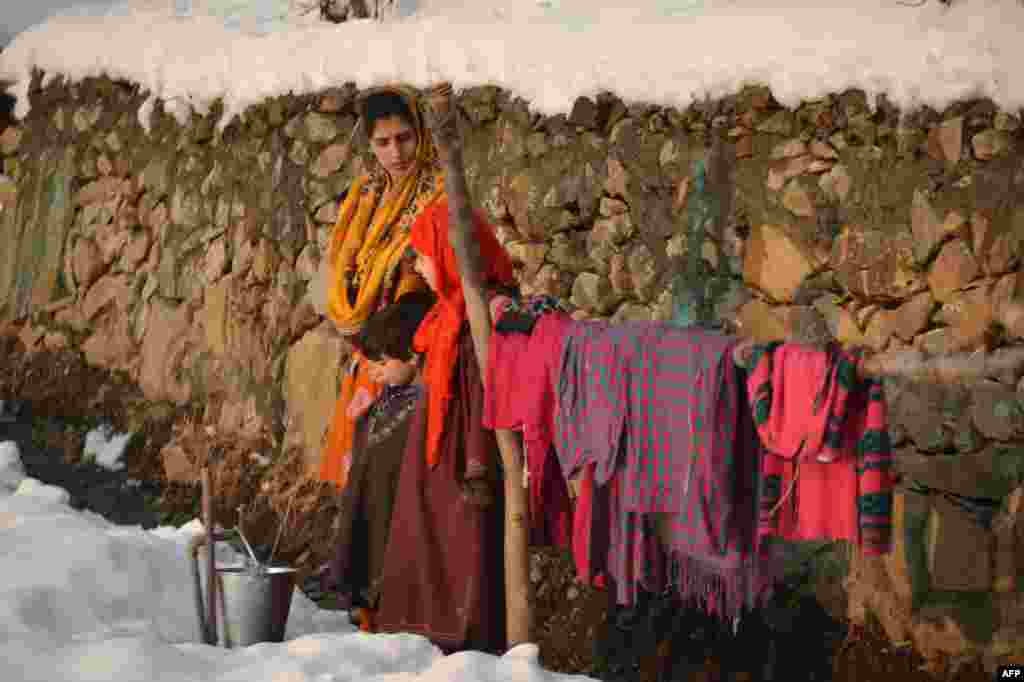 A Kashmiri woman waits as she fills water in an iron bucket on the outskirts of Srinagar, India, following the first snowfall of the season.