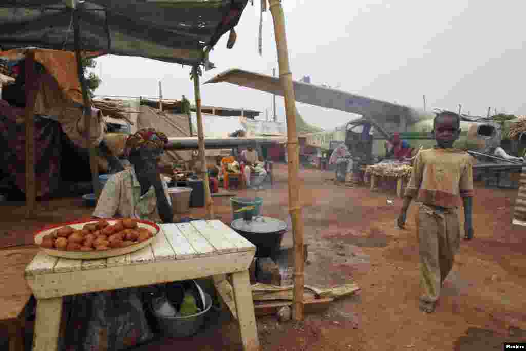 A boy displaced by inter-communal violence walks past a vendor in a camp for displaced persons at Bangui M'Poko International Airport, Feb. 11, 2014.