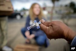 FILE - Marcelo Perez (R), an undocumented migrant from Mexico, shows his cross to volunteers dispensing donated goods to day laborers alongside a hardware store, Feb. 4, 2017, in San Diego, California.