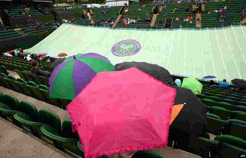 Spectators sit under umbrellas in No. 2 Court as it starts to rain on day five of the 2014 Wimbledon Championships at The All England Tennis Club in Wimbledon, southwest London.