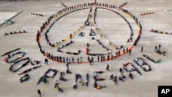 FILE - Environmental activists form human chains representing the peace sign and spelling out "100% renewable," on the sidelines of the 2015 Paris Climate Summit, near the Eiffel Tower in Paris, France, Dec. 6, 2015.
