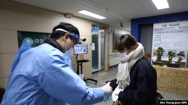 A teacher gives a hand sanitizer to a South Korean student before the College Scholastic Ability Test at a high school in Seoul Thursday, Nov. 18, 2021