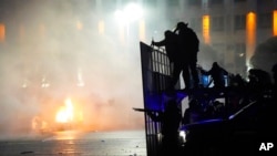 FILE - A police car burns as riot police prepare to stop protesters in the center of Almaty, Kazakhstan, Jan. 5, 2022. 