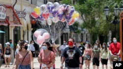Guests required to wear masks because of the coronavirus pandemic stroll through the Disney Springs shopping, dining and entertainment complex Tuesday, June 16, 2020, in Lake Buena Vista, Fla. Walt Disney World Resort theme parks plan to reopen on July 11
