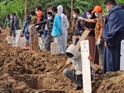 Seorang anak mendoakan anggota keluarga lainnya yang sudah dikuburkan di pemakaman khusus COVID-19 TPU Rorotan, Jakarta Utara. 8 Juli 2021 . (Foto:VOA/Indra Yoga)