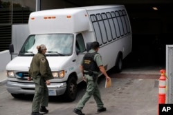 FILE - A van carrying asylum-seekers from the border is escorted by security personnel as it arrives at immigration court, in San Diego, March 19, 2019.