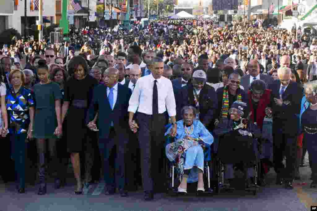 U.S. President Barack Obama, center, walks as he holds hands with Amelia Boynton Robinson, who was beaten during &quot;Bloody Sunday,&quot; along with the first family and others walk across the Edmund Pettus Bridge in Selma, Alabama, for the 50th anniversary of &ldquo;Bloody Sunday,&quot; a landmark event of the civil rights movement, March 7, 2015.