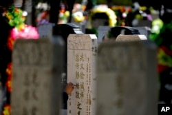 FILE - A woman repaints the characters that are carved in the tomb stone of her deceased relatives at the Babaoshan cemetery during the Qingming Festival in Beijing, April 3, 2016. (AP Photo/Andy Wong)