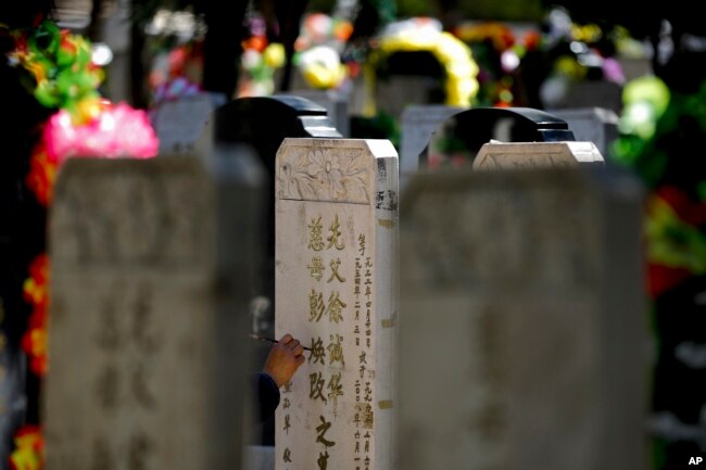 FILE - A woman repaints the characters that are carved in the tomb stone of her deceased relatives at the Babaoshan cemetery during the Qingming Festival in Beijing, April 3, 2016. (AP Photo/Andy Wong)