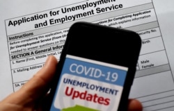 FILE - In this photo illustration, a COVID-19 Unemployment Assistance Updates logo is displayed on a smartphone on top of an application for unemployment benefits on May 8, 2020, in Arlington, Virginia.