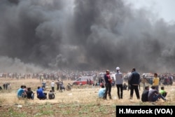 Tear gas hits people on the ground who are partially masked by smoke from tires that Palestinian protesters burn to create cover in Gaza, May 14, 2018.