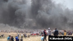 Tear gas hits people on the ground who are partially masked by smoke from tires that Palestinian protesters burn to create cover in Gaza, May 14, 2018.