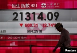 A man walks past a panel displaying the benchmark Hang Seng index during afternoon trading in Hong Kong, China, Jan. 4, 2016.