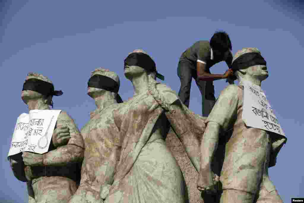 A student activist puts black scarves on the eyes of Shoparjito Shadhinota, a sculpture that represented all sections of people in Bangladesh&#39;s liberation War in 1971,&nbsp; in the campus of University of Dhaka, to demand capital punishment for Jamaat-e-Islami senior leader Abdul Quade after a war crimes tribunal sentenced him to life imprisonment.