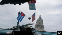 Miniatur bendera nasional Kuba dan Amerika Serikat menghiasi sebuah taksi yang melewati Gedung Capitol di Havana, Kuba. (Foto: Dok)