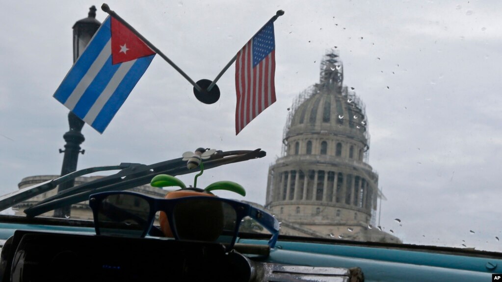 Banderas de Cuba y Estados Unidos decoran el interior de un automÃ³vil estadounidense clÃ¡sico utilizado como taxi que pasa por el Capitolio de La Habana, Cuba, el viernes 16 de enero de 2015.