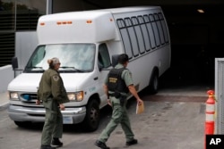 FILE - A van carrying asylum seekers from the border is escorted by security personnel as it arrives to immigration court, in San Diego, California, March 19, 2019.