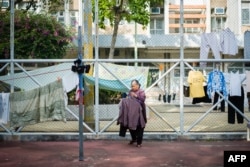 An elderly woman collects items of laundry that were hung out to dry along fences in a playground of a government housing estate in Hong Kong, Dec. 20, 2018.