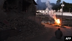 A Nepalese man sits near a collapsed wall and a burning pyre with the mortal remains of earthquake victim Sushila Thami at an open air crematorium in Kathmandu on May 5, 2015, after her body was brought from Dolakha. 