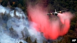 A firefighting plane drops a load of fire retardant over a smoldering hillside, Sept. 15, 2015, in Middletown, Calif.