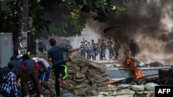 A protester (centre L) throws a projectile towards security forces as others shelter behind a barricade during a crackdown on protests against the military coup in Yangon on March 17, 2021. (Photo by STR / AFP)