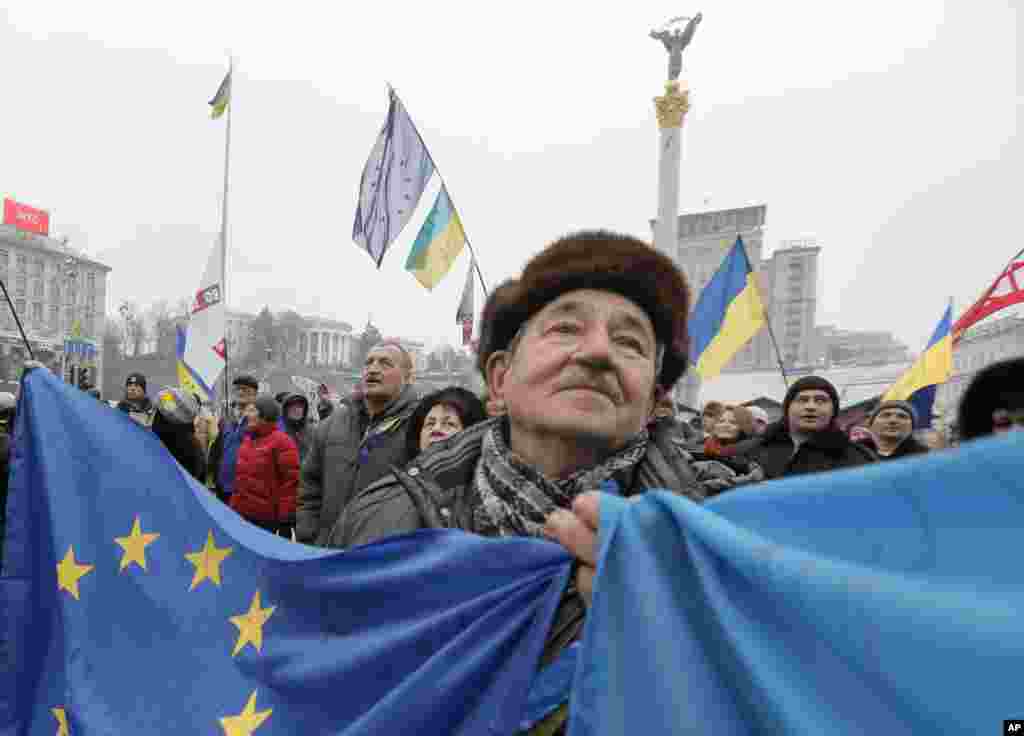 A pro-European Union activist with Ukrainian and the European Union flags stands with others in Independence Square in Kyiv, Ukraine. 