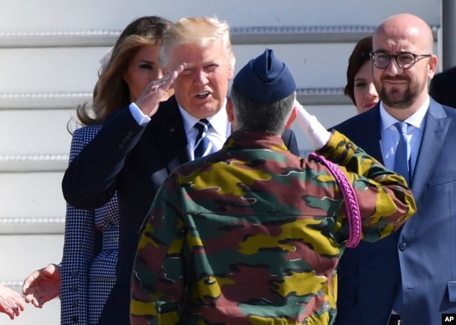 US President Donald Trump, second left, salutes a Belgian soldier as he arrives at Melsbroek Military Airport in Belgium, May 24, 2017. At right is Belgian Prime Minister Charles Michel.