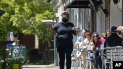 Seorang anggota staf mengantarkan makanan untuk pengunjung yang duduk di luar ruangan di sepanjang trotoar restoran Mediterranean Deli di Chapel Hill, North Carolina, 16 April 2021. (AP Photo/Gerry Broome)