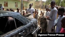 FILE - The wreckage of a car hit by an attack by Boko Haram fighters is seen surrounded by residents in the Adam Kolo district of Maiduguri, Nigeria, Feb. 24, 2021.