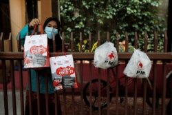 Seorang ibu yang sedan menjalani isolasi mandiri bersama suaminya yang terinfeksi Covid-19, mengambil paket bantuan yang diletakkan di pagar rumah mereka di Jakarta, 3 Agustus 2020. (Foto: Willy Kurniawan/Reuters)