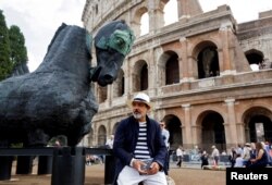 Mexican artist Gustavo Aceves sits next to a sculpture at Rome's Colosseum during his art exhibition called "Lapidarium, Waiting for the Barbarians" in Rome, Italy, Sept. 15, 2016.