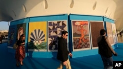 FILE - Onlookers walk by a collection of Olympic posters made by 12 Brazilian artists and a Colombian, on display at the Museum of Tomorrow in Rio de Janeiro, Brazil.