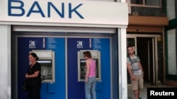 People make transactions at ATM machines outside a bank branch in Athens, Aug. 12, 2013.