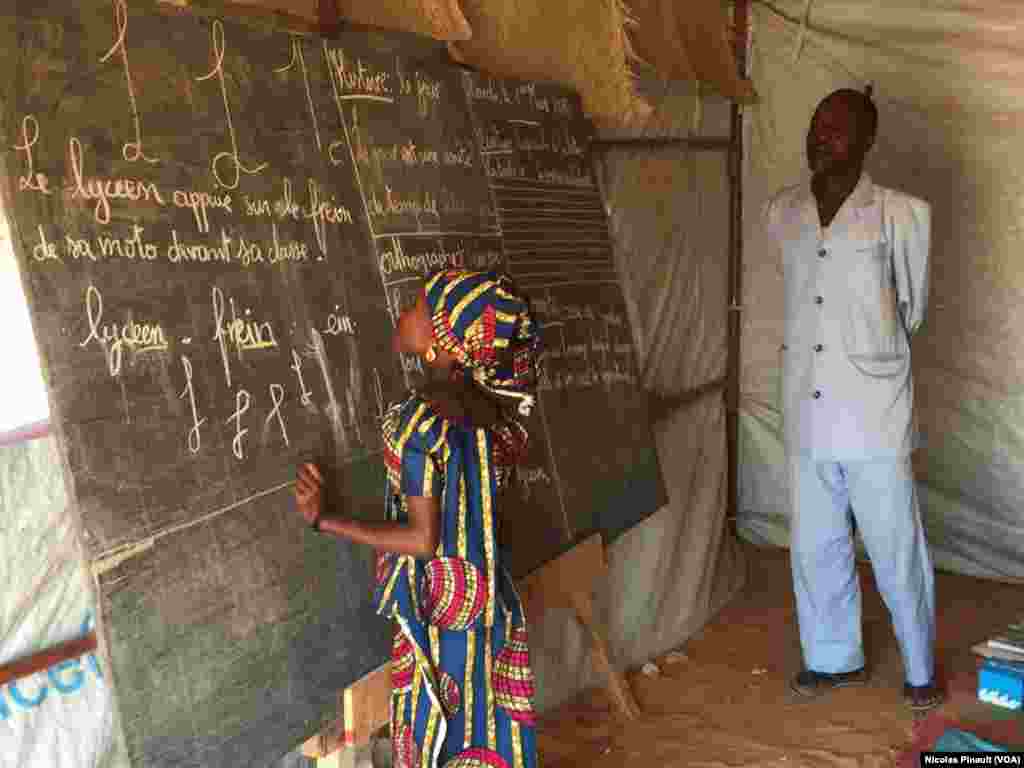 Une élève de 10 ans écrit sur le tableau d'une salle de classe provisoire dans le camp de Ngourtoua, près de Diffa, au Niger, le 1er mars 2016. (VOA/Nicolas Pinault)