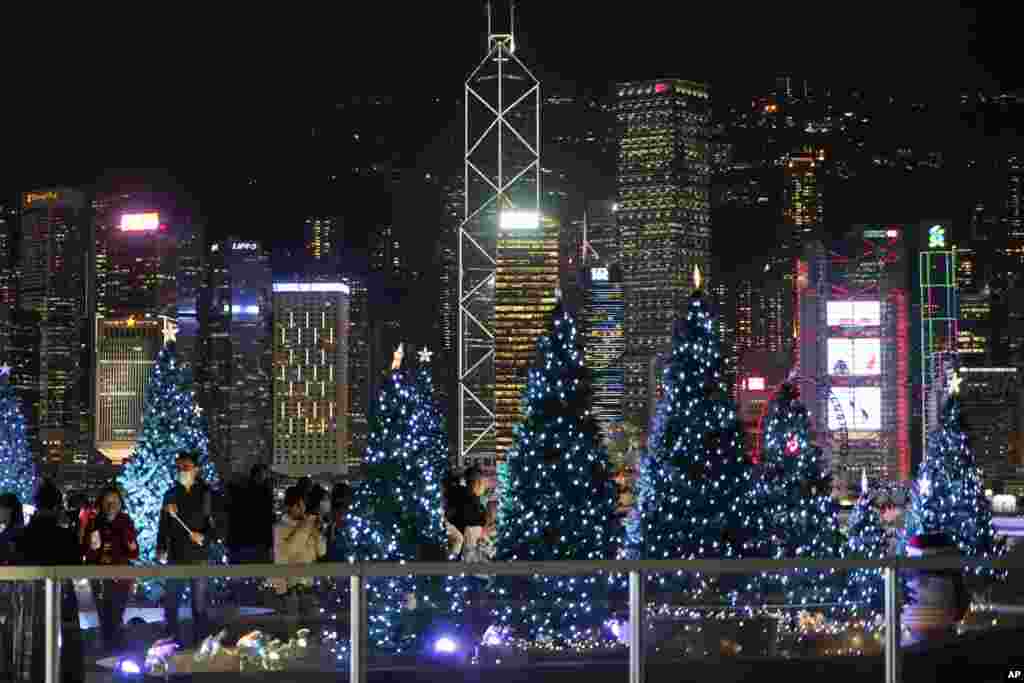 People wearing protective masks take photographs of Christmas trees and holiday decorations in Hong Kong.