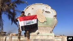 An Iraqi soldier holds a national flag atop the government complex in central Ramadi, Iraq, Dec. 28, 2015. 