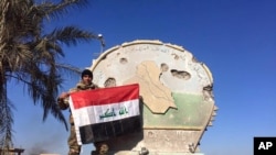 An Iraqi soldier holds a national flag atop the government complex in central Ramadi, Iraq, Dec. 28, 2015. 