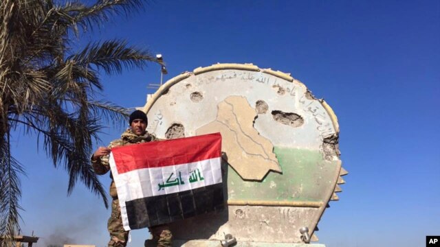Un soldado iraquí sostiene la bandera nacional en el complejo de gobierno en Ramadi, al occidente de Bagdad. Dic. 28 de 2015.