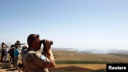 A United Nations peacekeeping soldier uses binoculars to watch fighting between forces loyal to and opposed to Syrian President Bashar al-Assad, from the Golan Heights, June 7, 2013.