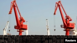 FILE - Piles of steel pipes to be exported are seen in front of cranes at a port in Lianyungang, Jiangsu province, March 7, 2015. 