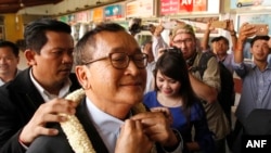 FILE - Sam Rainsy, foreground, leader of the opposition Cambodia National Rescue Party (CNRP), receives a garland of jasmine upon his arrival at Phnom Penh International Airport in Phnom Penh, Cambodia, Aug. 16, 2015.