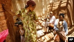FILE - Malagasy women and children wait in the shade at a makeshift village clinic in Antanetikely, Madagascar, Oct. 23, 2007.