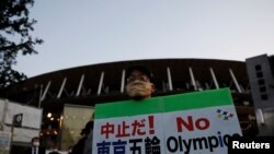 Seorang pengunjuk rasa yang menuntut pembatalan Olimpiade Tokyo 2020 memegang spanduk di depan Stadion Nasional, stadion utama Olimpiade dan Paralimpiade Tokyo 2020. (Foto: Reuters)
