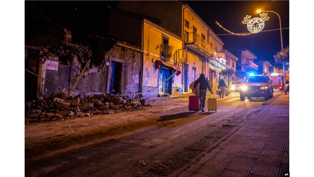 A man carries his belongings as he walks past debris of a partially collapsed house in Fleri, Sicily, Dec. 26, 2018.